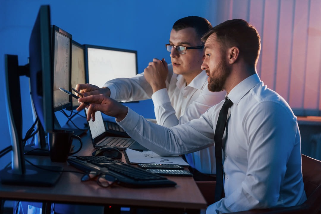 Dois homens sentados em frente a um computador enquanto discutem estratégias de FinOps.